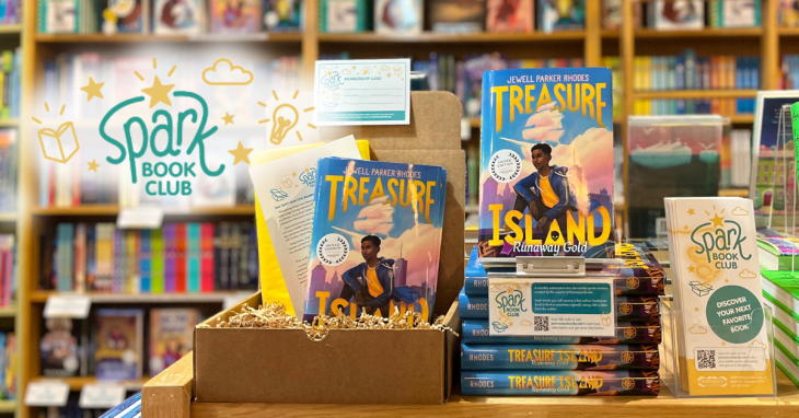 A stack of Treasure Island: Runaway Gold by Jewell Parker Rhodes next to one of our Spark subscription boxes, which is stuffed with crinkle paper and has the book wrapped in yellow tissue paper inside